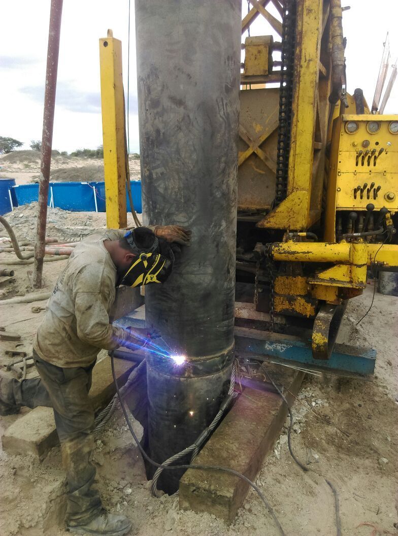 Un soldador suelda un tubo de metal cerca de un equipo de construcción al aire libre.