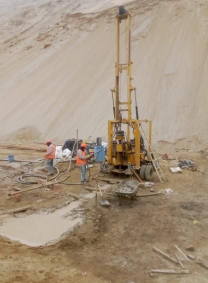 Los trabajadores operan una plataforma de perforación amarilla en una cantera polvorienta y arenosa. Dos de ellos llevan chalecos naranjas.