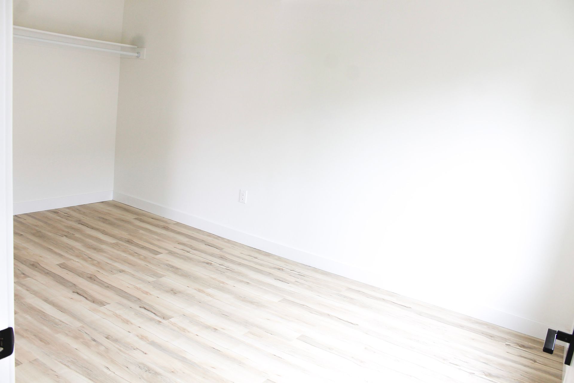 Empty closet with wood-look flooring and white walls. A metal shelf is visible at the top.