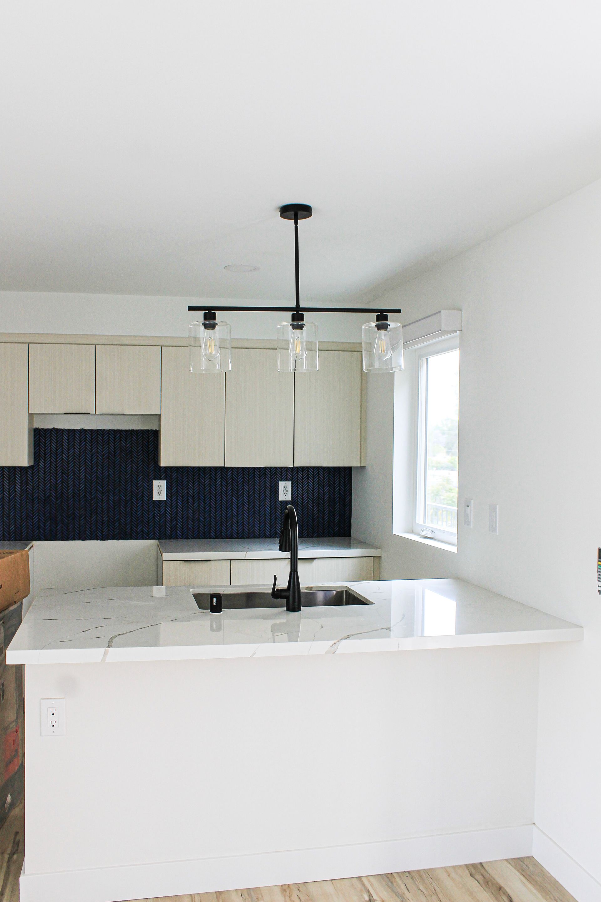 Modern kitchen with white countertops, black faucet, and blue tiled backsplash.