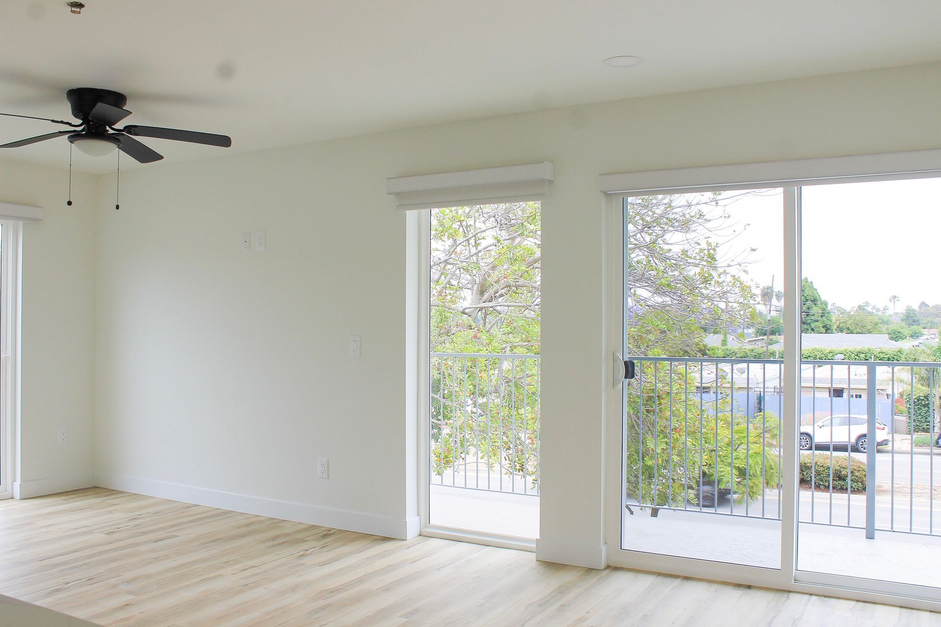 Bright, empty room with large windows and a ceiling fan. Beige floor, white walls.