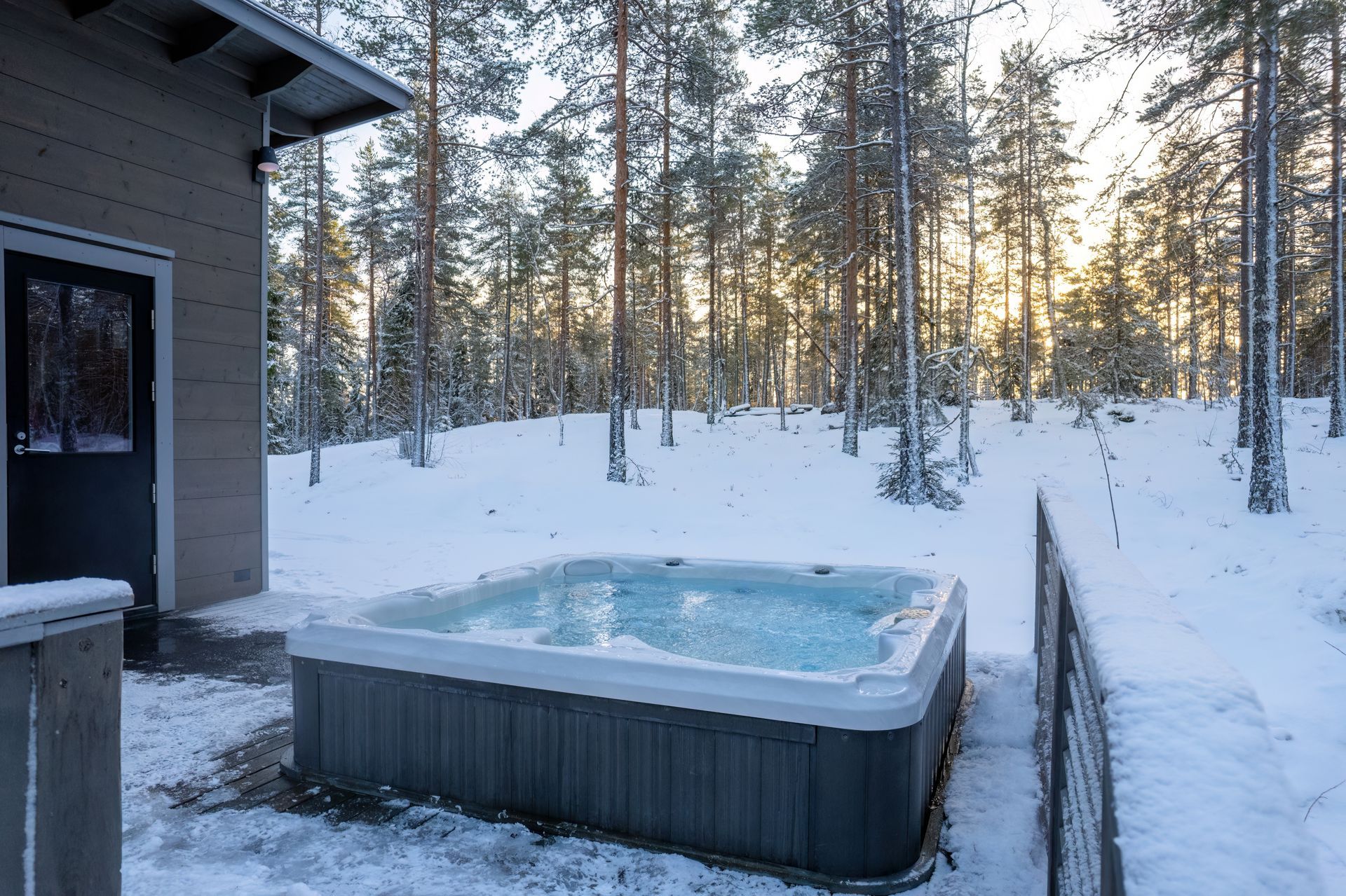 A hot tub is sitting in the snow in front of a house.
