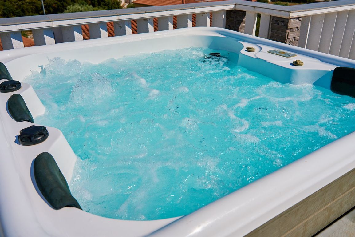 A white hot tub filled with blue water on a balcony.