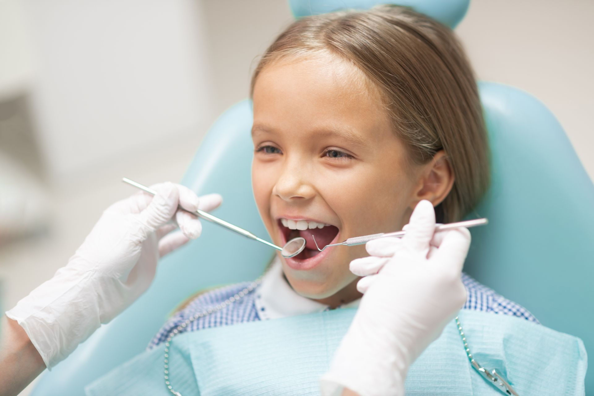Girl at dentist, mouth open, being examined with tools in a dental chair.