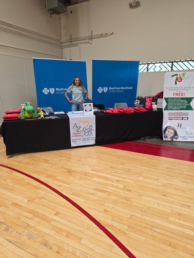 A woman stands behind a table in a gymnasium. The table is covered with promotional materials.