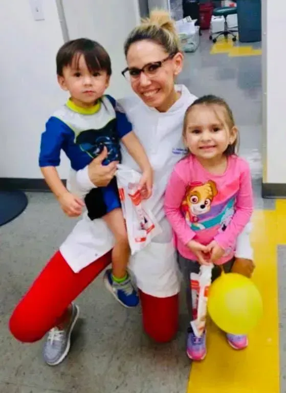 Woman kneeling, holding a boy and smiling at the camera next to a girl with a balloon.