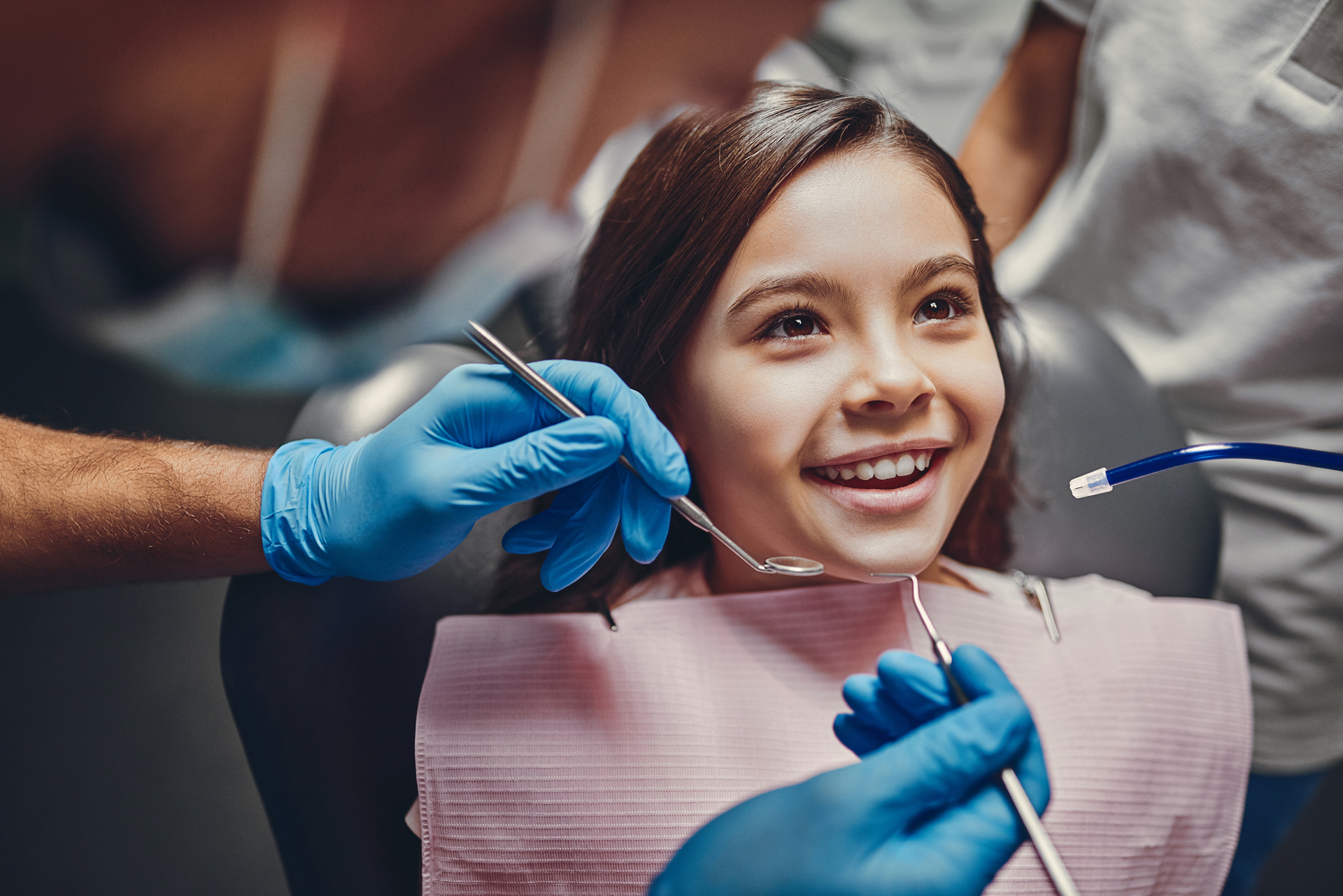 Smiling girl at dentist, dental tools, blue gloves, pink bib, dentist's office.