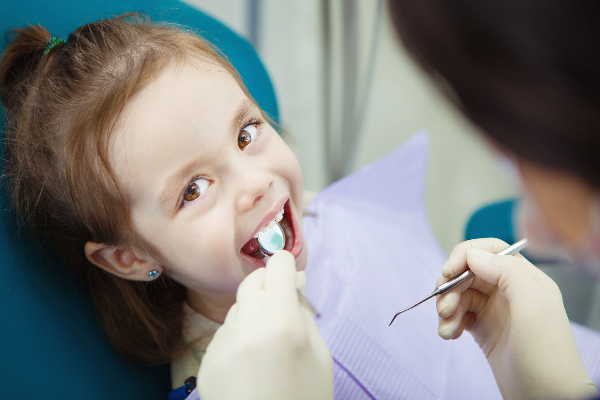 Child getting a dental checkup: girl in chair, dentist using tools, smiling.