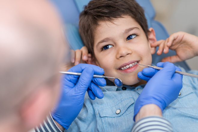 Boy in a dentist's chair having teeth examined by a dentist wearing blue gloves.