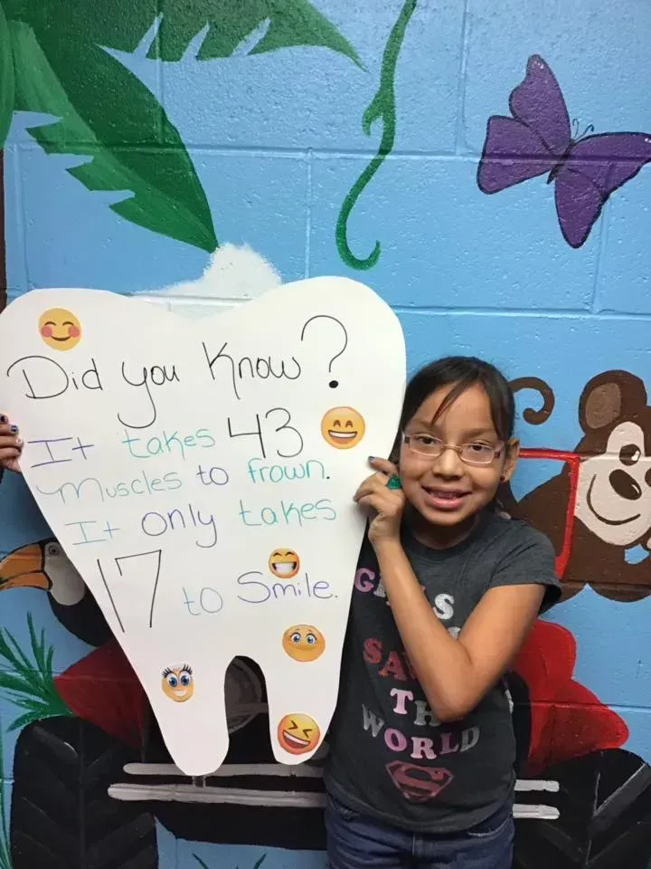 Girl with glasses points to a tooth-shaped sign: