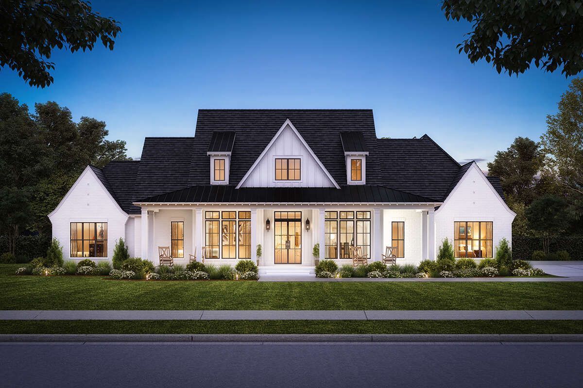 A large white house with a black roof is sitting on top of a lush green lawn.