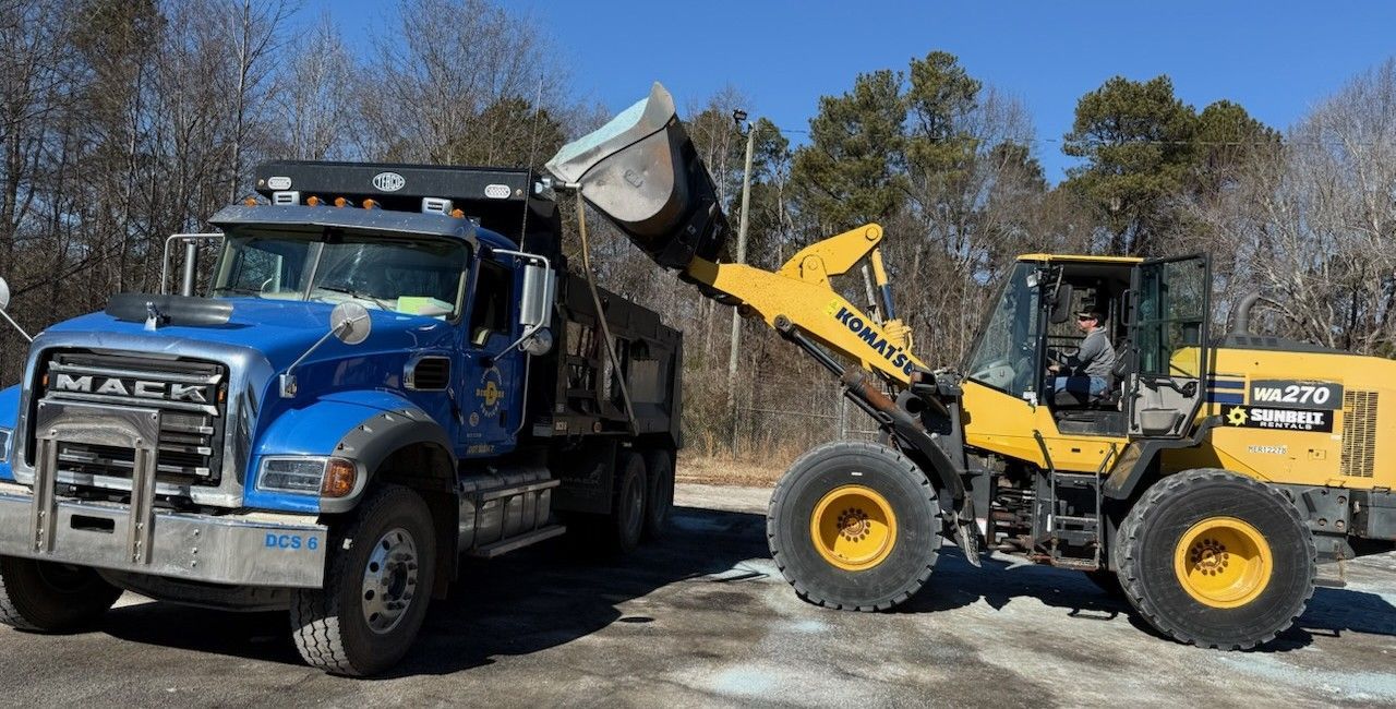 A blue dump truck being loaded with material by a yellow front-end loader in an outdoor setting.