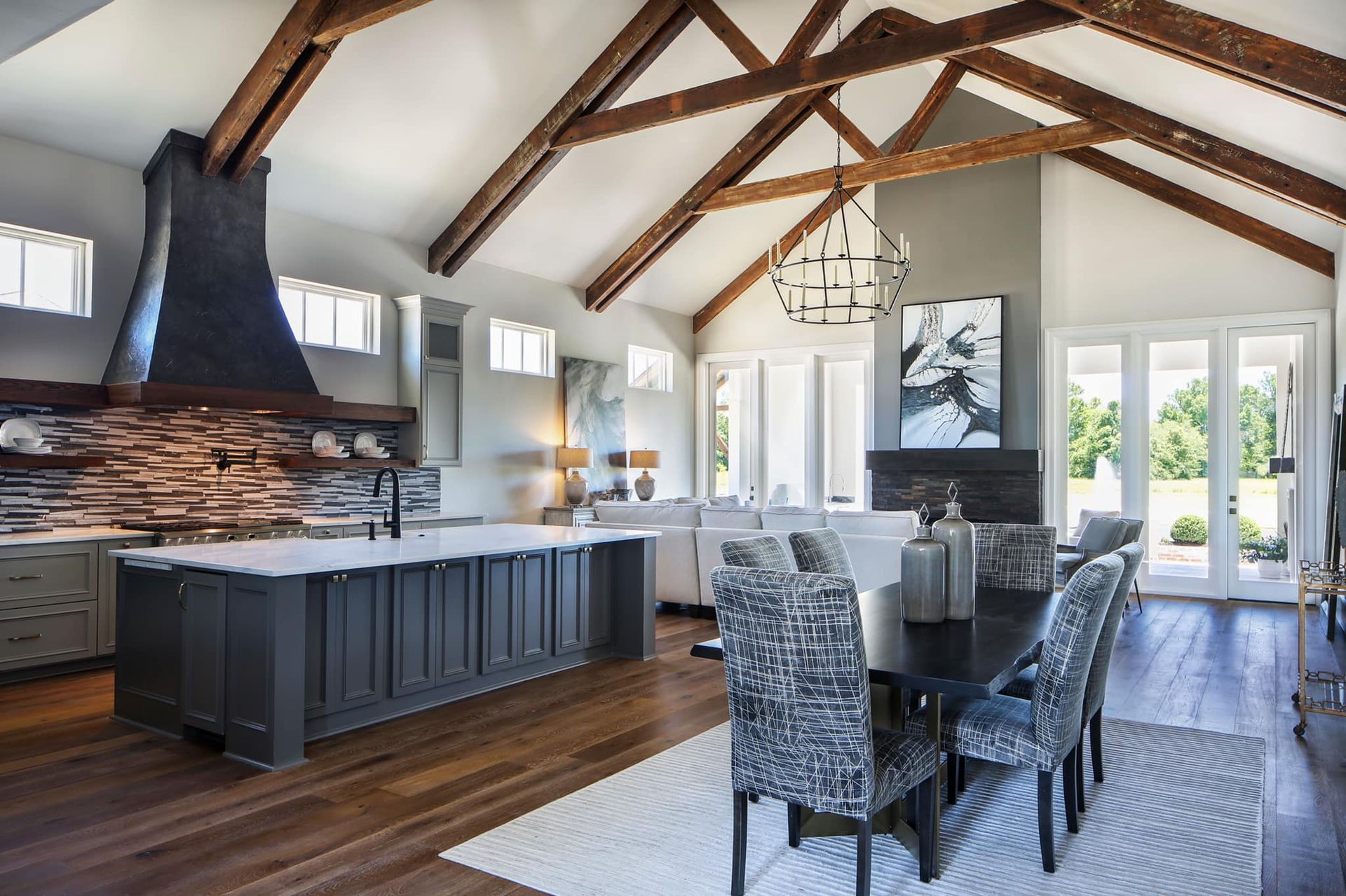 Spacious kitchen and dining room with exposed beams, dark island, and gray walls.