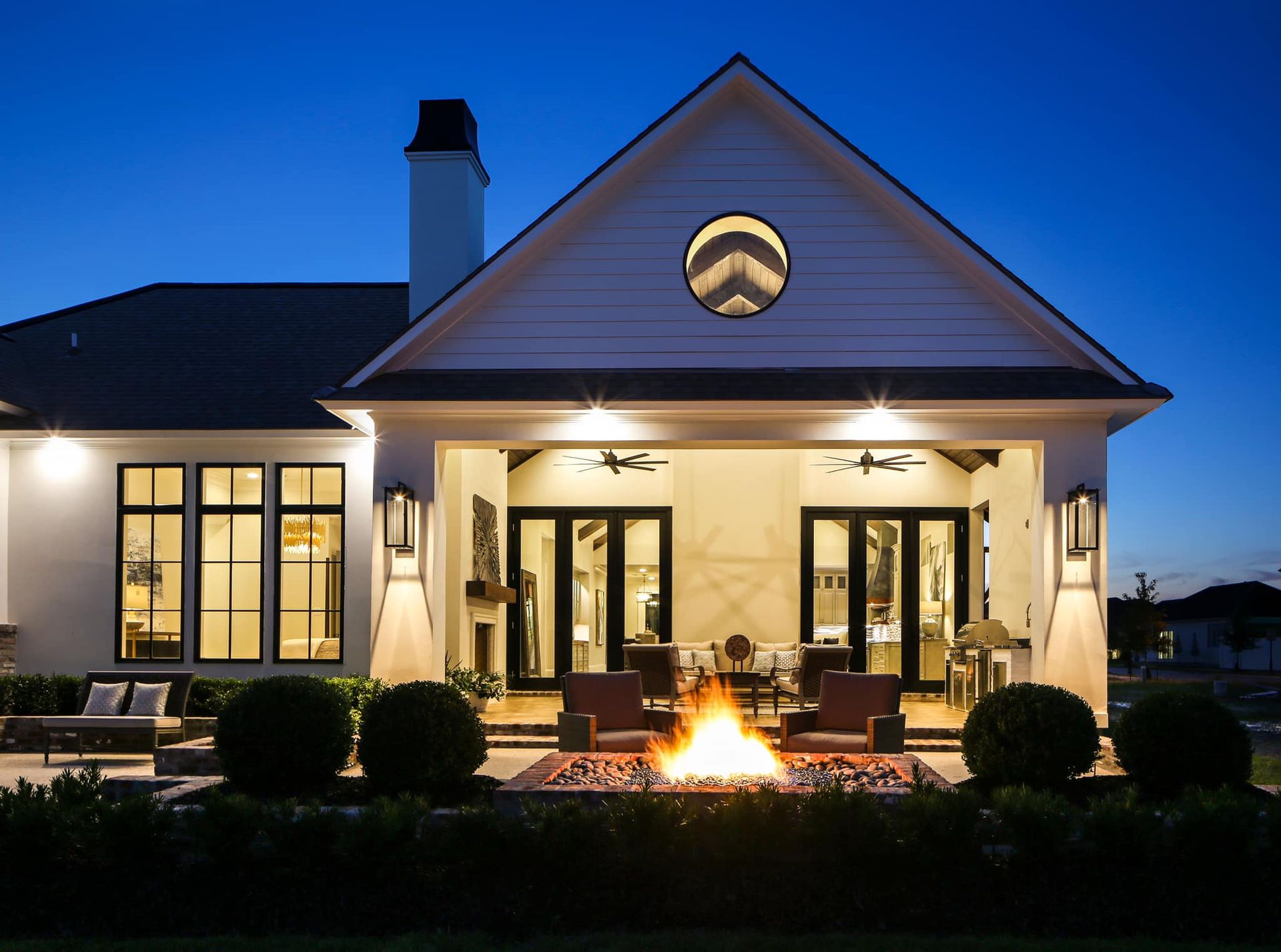 Backyard patio with a fire pit under a white-painted house at dusk.