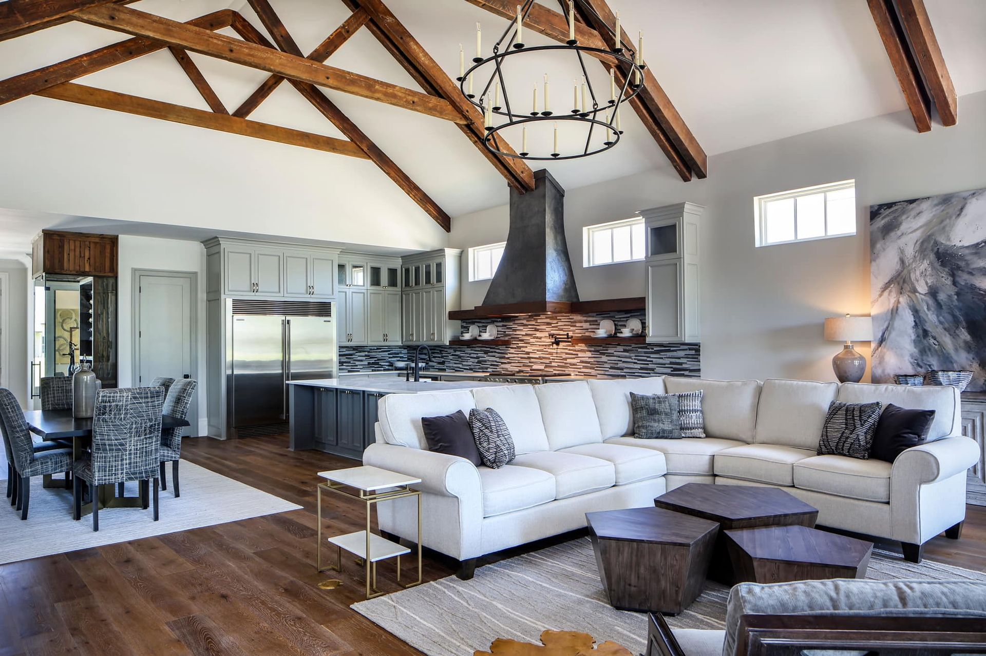 Open-concept living space with a kitchen, dining area, and seating. White couch, wooden beams, and a modern light fixture.
