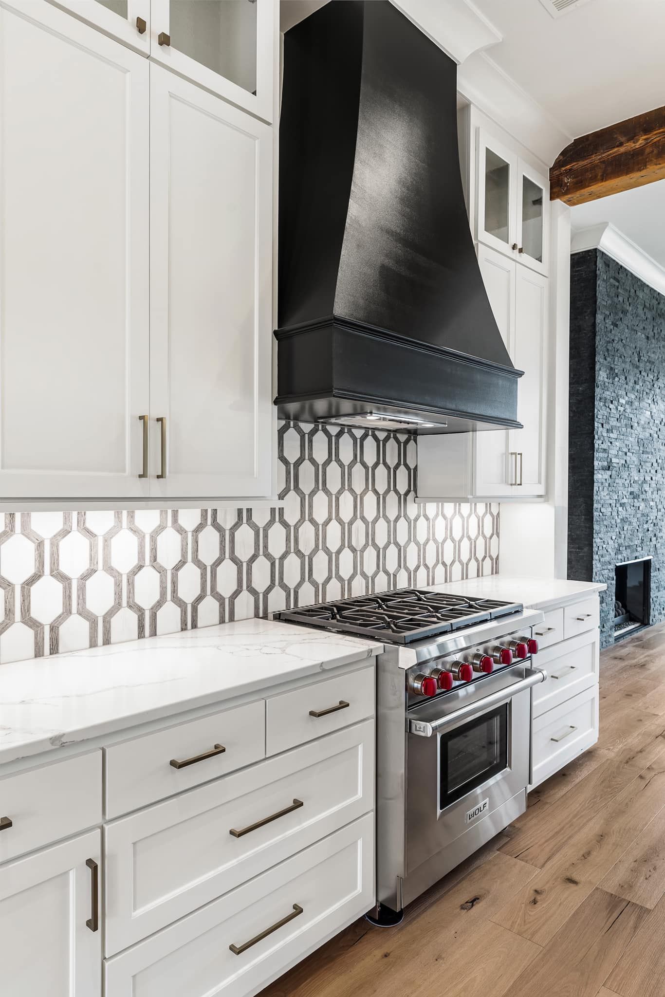 White kitchen with stove and black hood. Geometric backsplash and light cabinets.