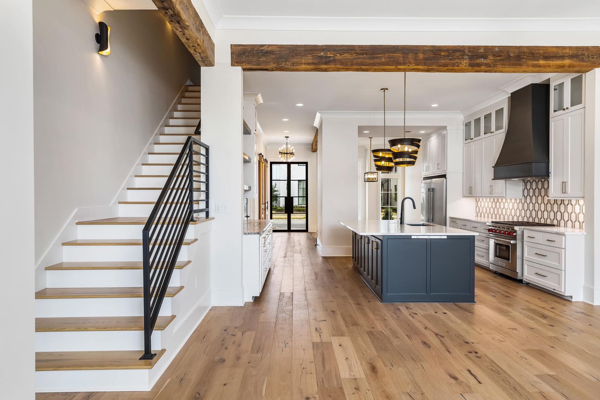 Open-concept kitchen and staircase with wooden floors, white cabinets, and a dark blue island.