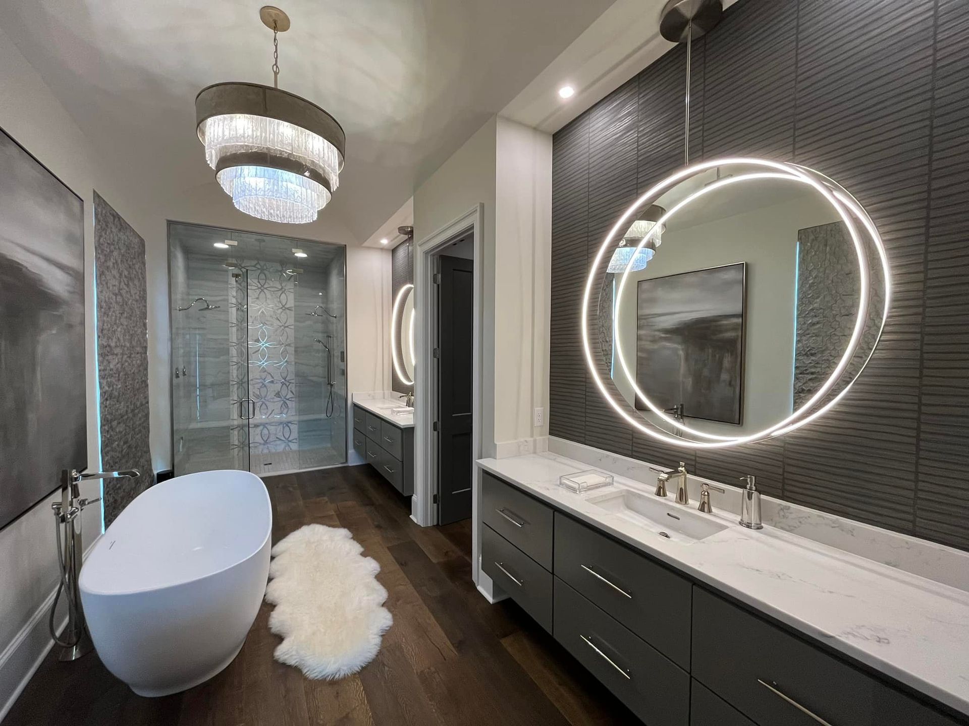 Modern bathroom with gray vanity, backlit mirror, and a freestanding tub.