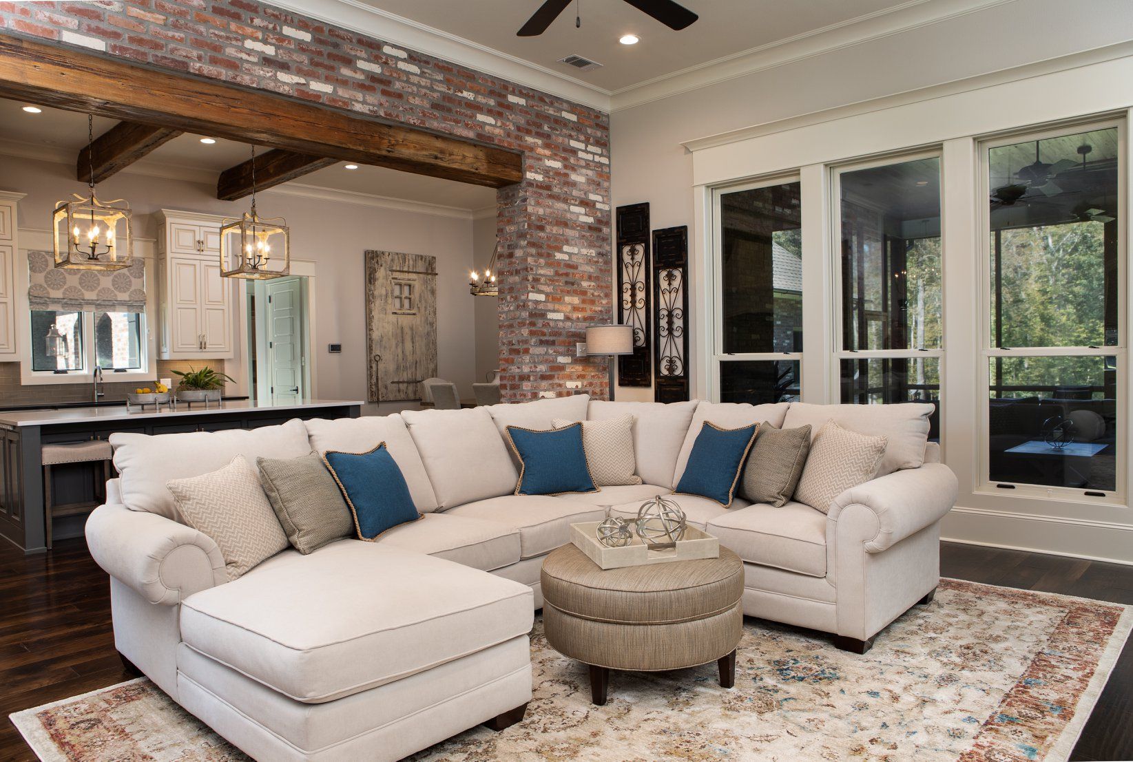 Living room with white sectional sofa, ottoman, and brick wall.