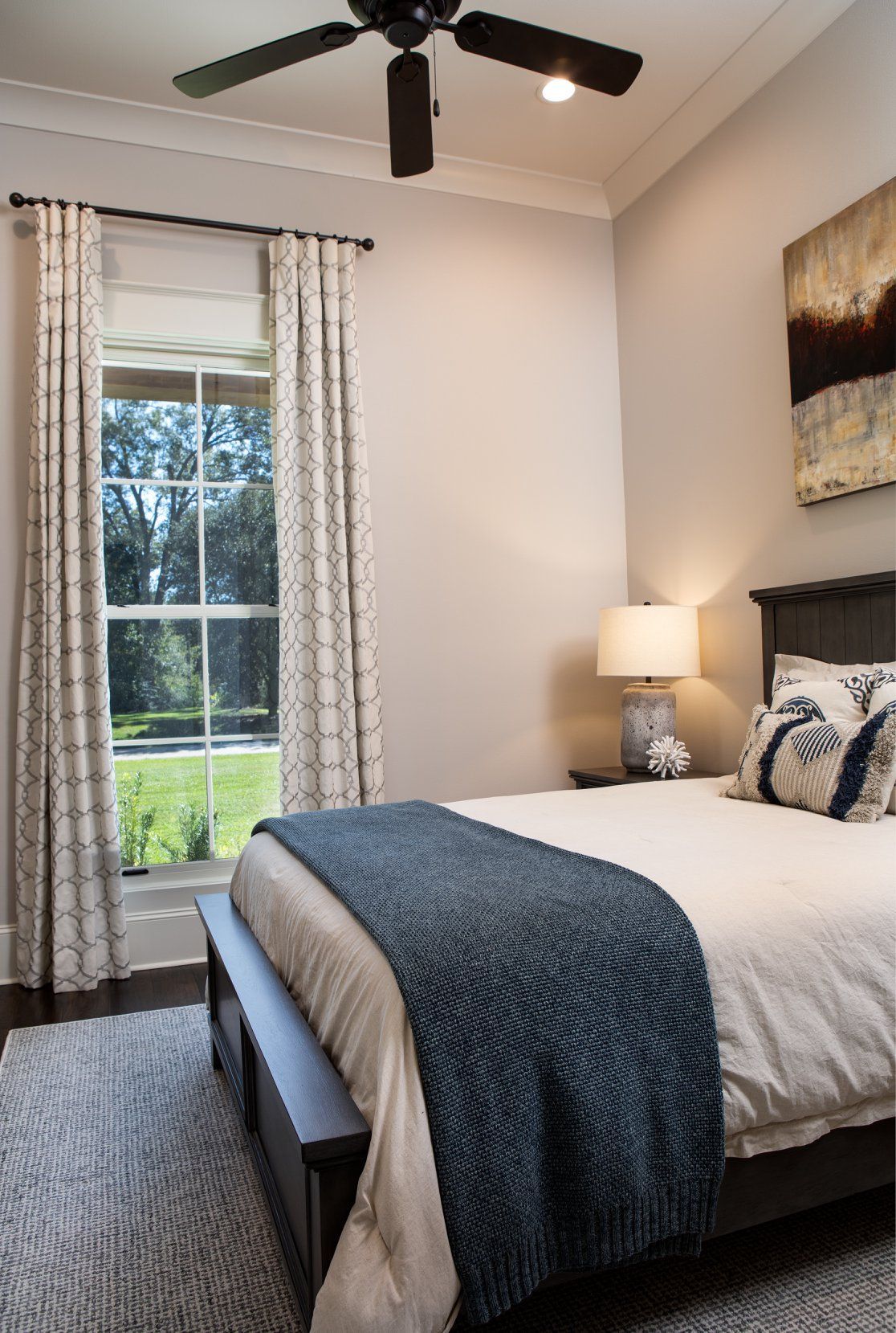 Bedroom with bed, window, curtains, ceiling fan, and artwork on wall.