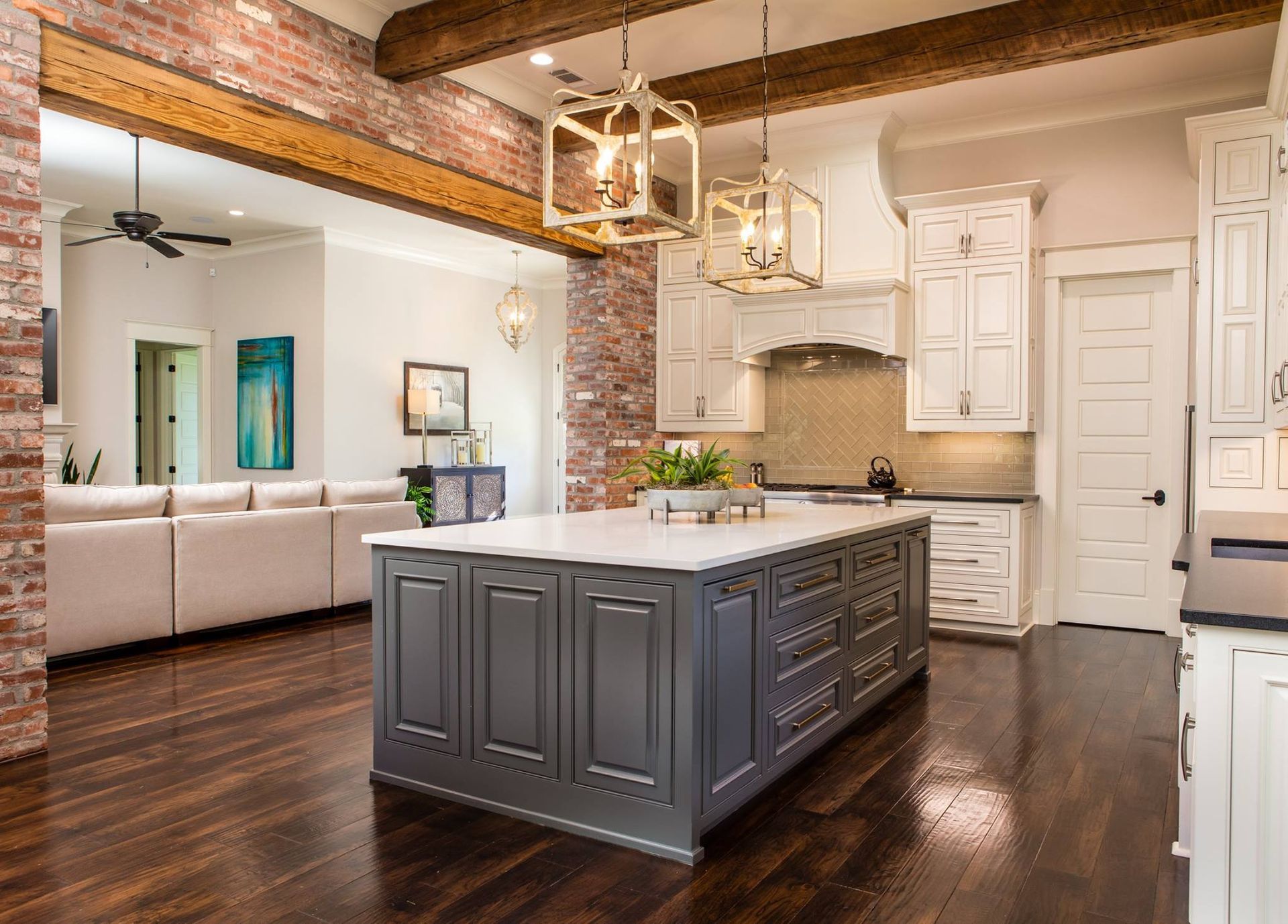 Kitchen with a large island, exposed brick, hardwood floors, and open view to a living room.