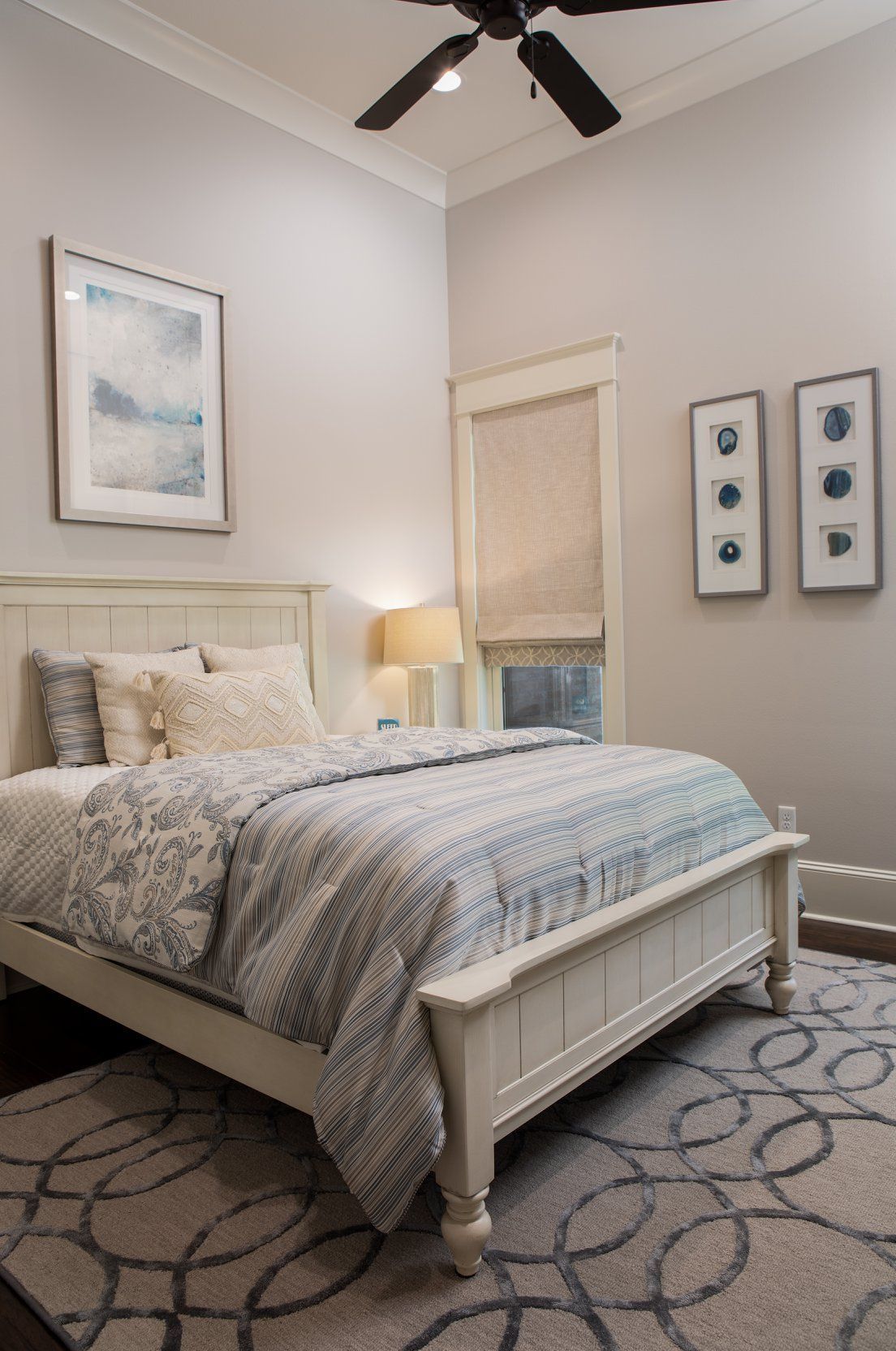 Bedroom with white bed, gray bedding, art, window, and patterned rug.