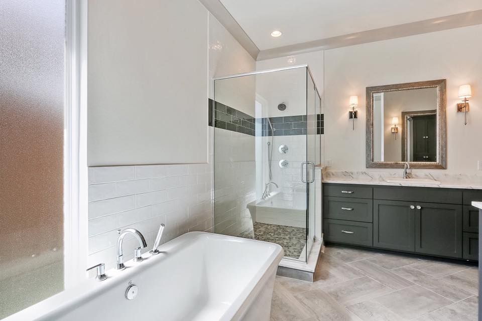 Bathroom with a glass shower, bathtub, dark gray vanity, and marble countertops.