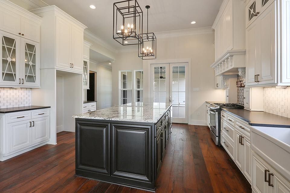 Elegant white kitchen with dark island, granite countertop, hardwood floors, and a chandelier.