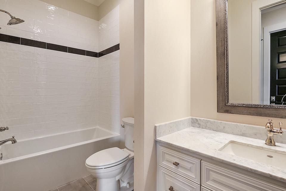 Bathroom with white tile, bathtub, toilet, vanity, and mirror.