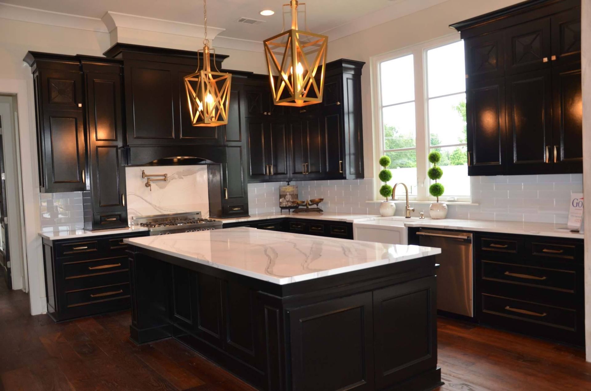 Black kitchen with white countertops, island, and gold pendant lights.