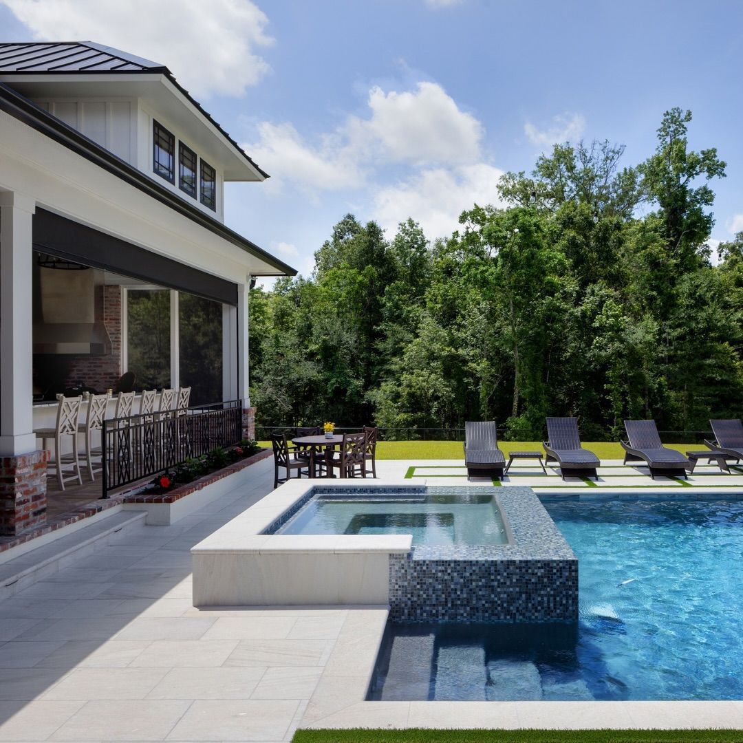 Backyard with pool, hot tub, and outdoor dining under a white house. Green grass and trees surround.