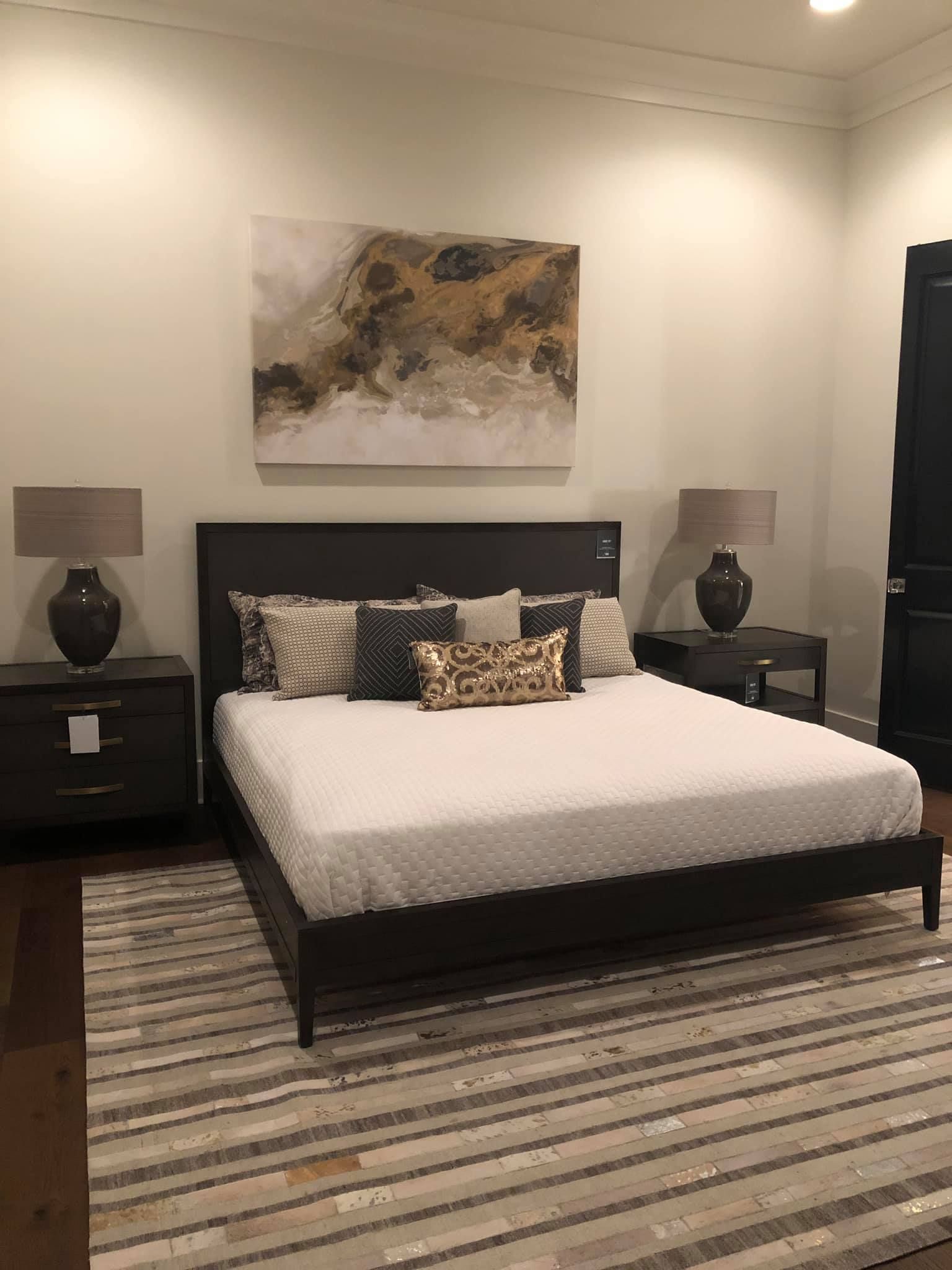 Bedroom with bed, nightstands, lamps, art, and rug on wooden floor.