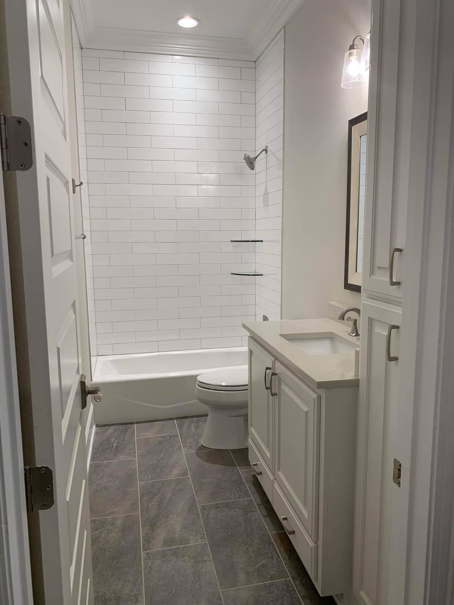A white bathroom with textured tile in the shower, white vanity, and dark gray flooring.