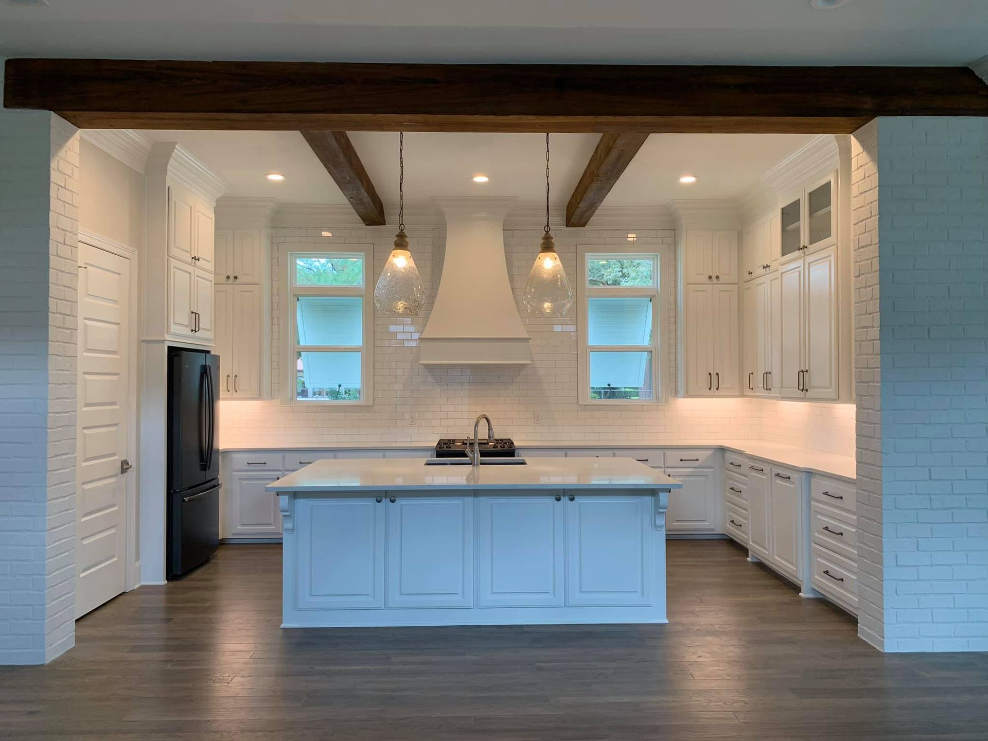 White kitchen with island, wooden beams, and black appliances.