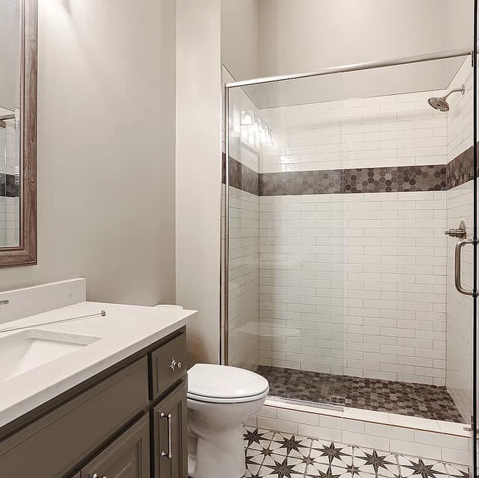 Bathroom with white subway tile shower, grey vanity, and patterned floor.