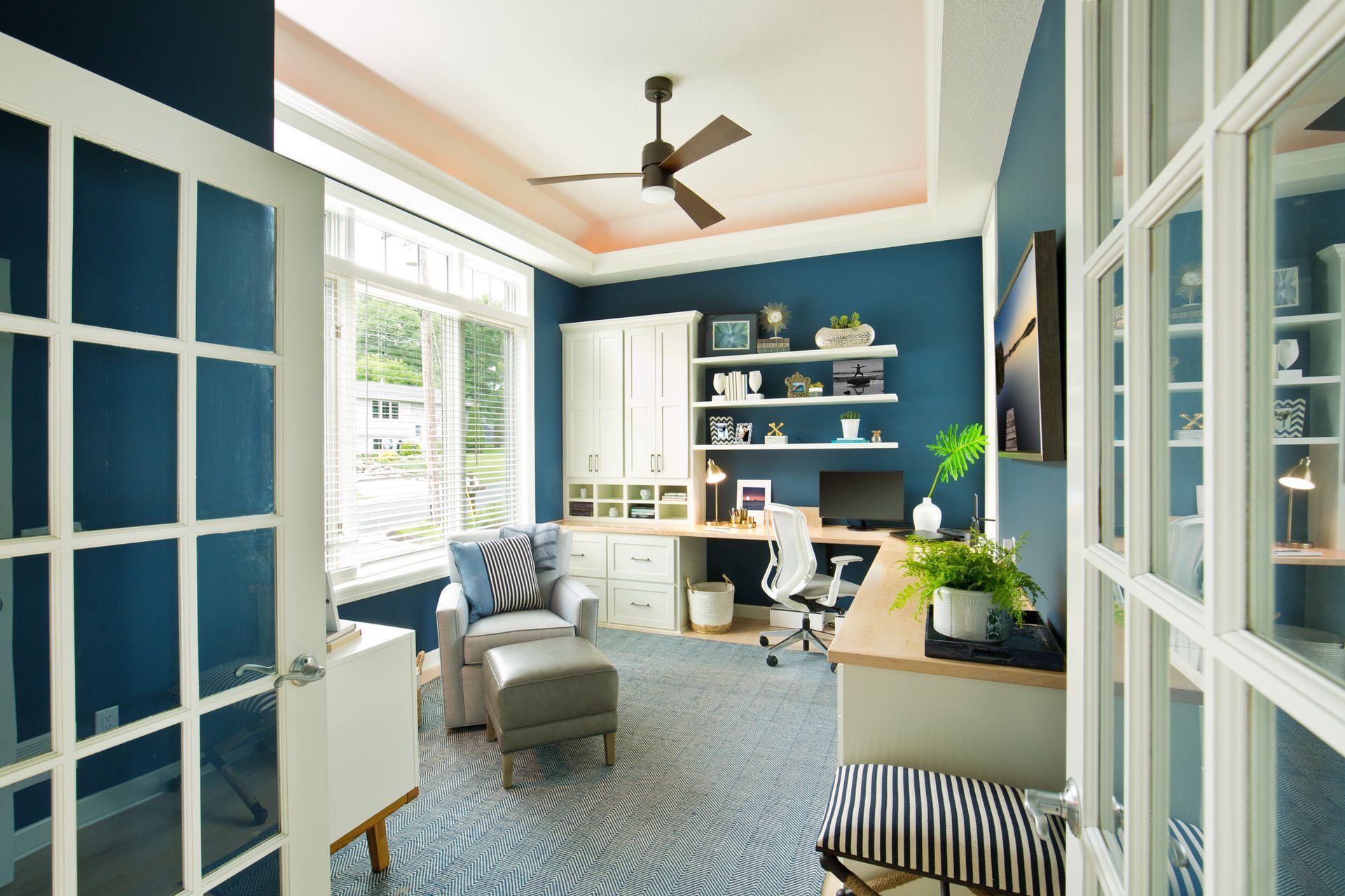 Home office with blue walls, pink ceiling, large window, desk, and armchair.