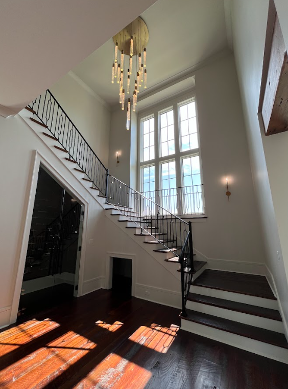 A modern kitchen with a wooden floor, white cabinets, granite countertops, and a hallway leading to a glass front door.