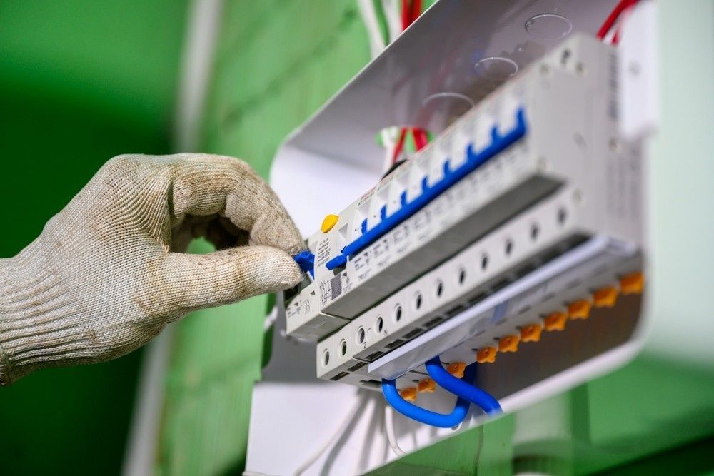 Hand Flipping an Electrical Circuit Breaker in A White Panel — Messina Air Conditioning & Electrical in Kuranda, QLD