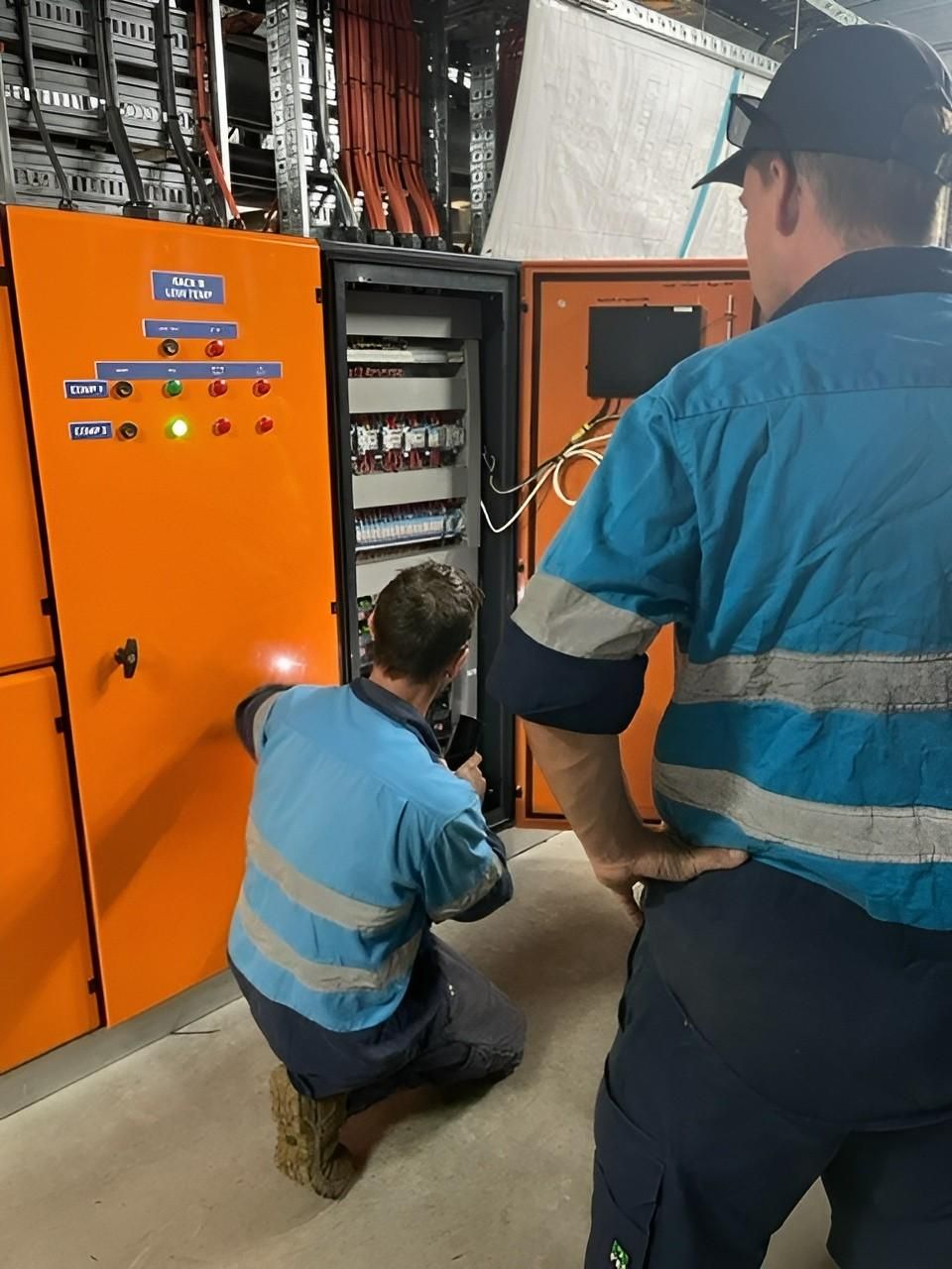 Workers in Blue Shirts Inspecting an Orange Electrical Panel — Messina Air Conditioning & Electrical in Portsmith, QLD