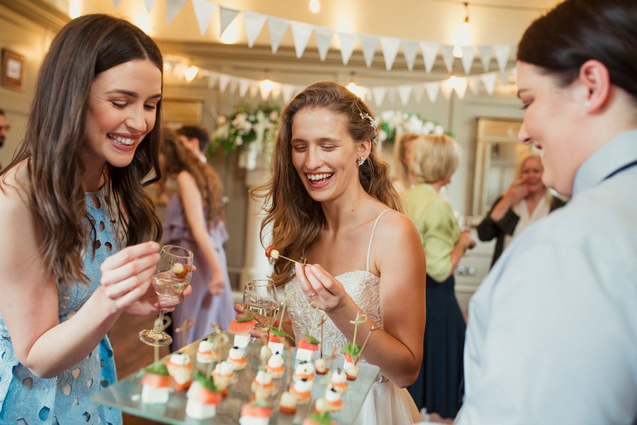 A group of women are standing around a table eating food at a wedding reception.