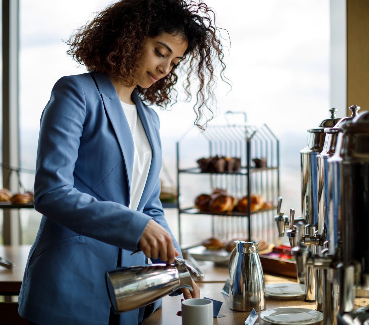 A woman in a blue jacket is pouring coffee into a cup.