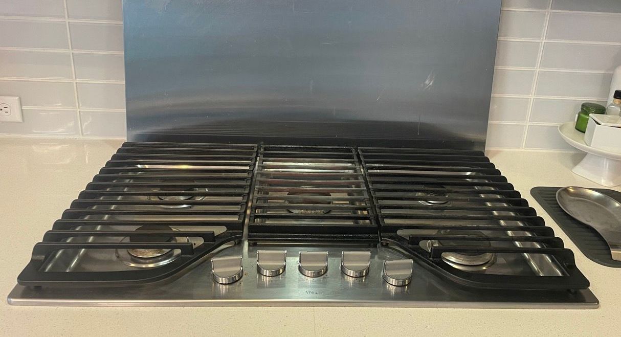 Black gas stovetop with four burners and control knobs, set against a tiled kitchen backsplash.