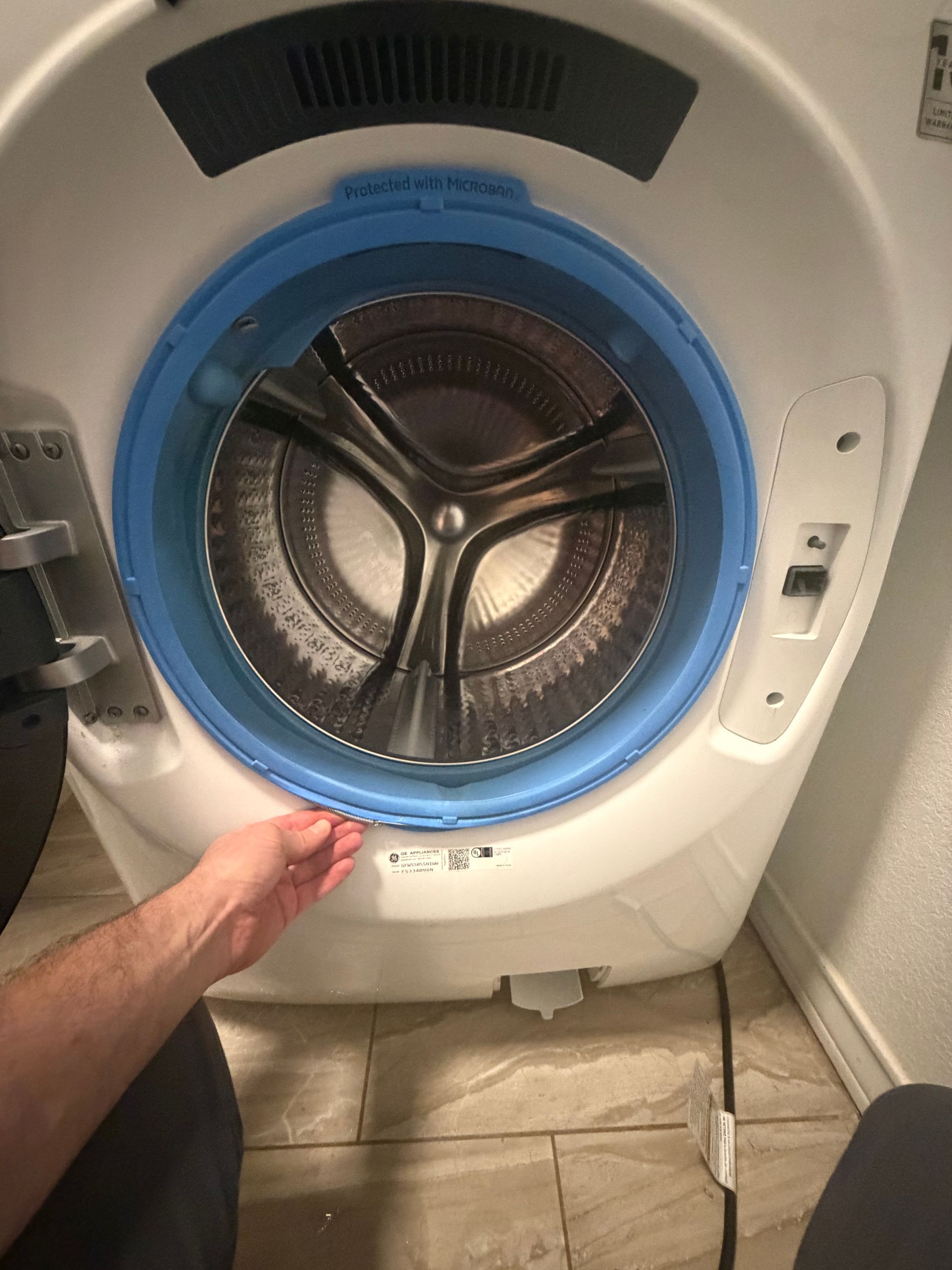 Hand reaching to open a blue front-load dryer with clothes inside in a laundry room