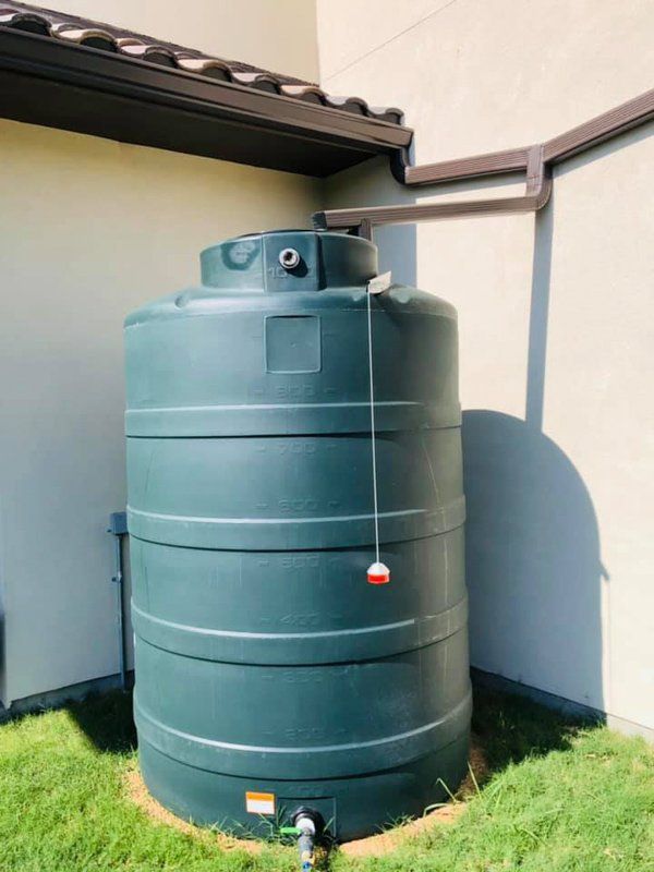 a large green water tank is sitting in the grass next to a building .