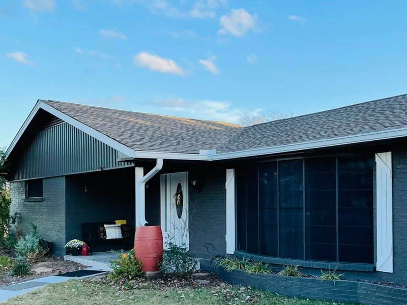 a black house with a screened in porch and a blue sky in the background .
