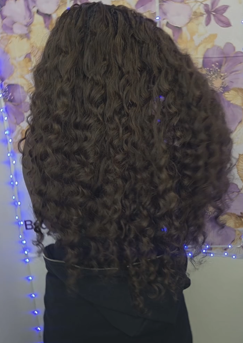 Woman with long, curly, brown hair, back view. Wearing a black hooded sweatshirt.