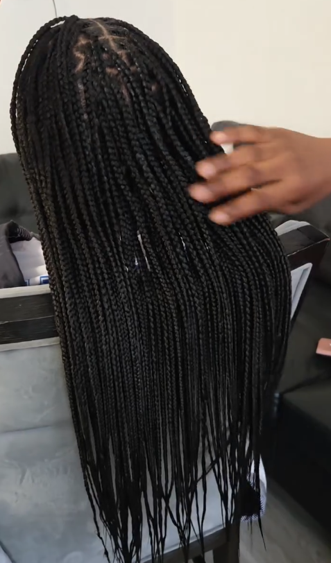 Black braided wig on a mannequin; a hand gently touches the hair.