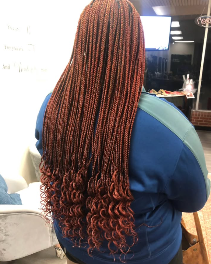 Woman with long, auburn-colored braids cascading over a blue sweatshirt. Curly ends.