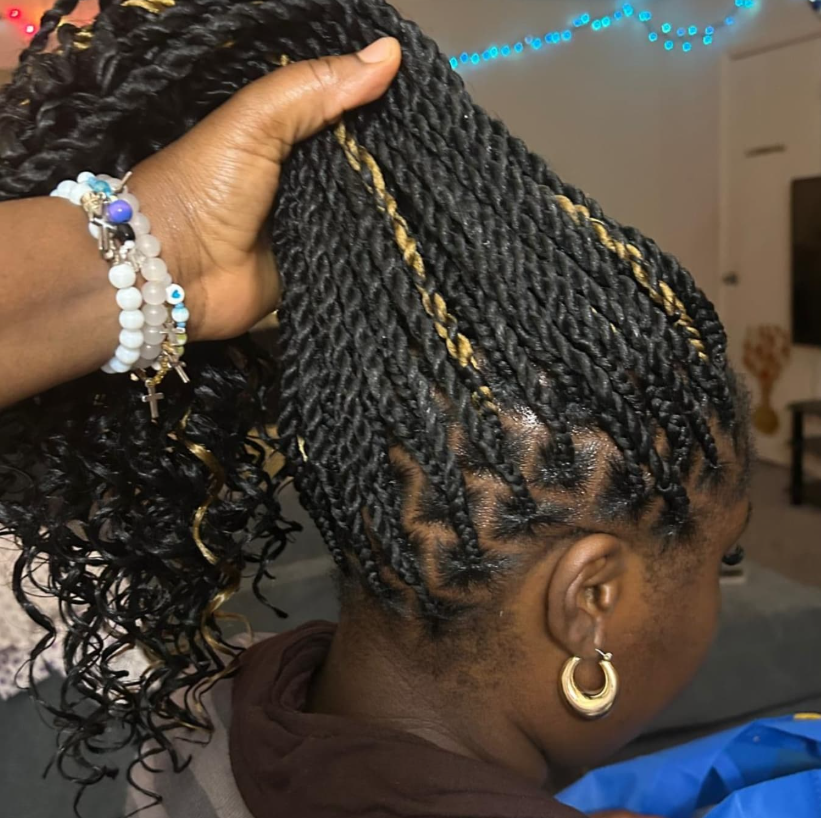 Person with black twisted braids being styled, with golden earrings. Braids have blonde highlights. Hand holding up hair.