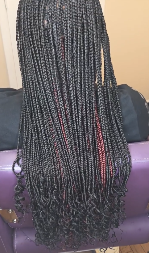 Black box braids with curly ends, some red highlights, resting on a purple surface.
